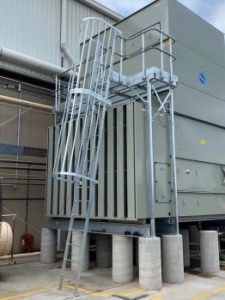 Close-up of an industrial cooling tower showing a fixed metal ladder with a safety cage leading to a raised access platform for safe maintenance and inspection.