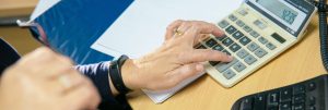 A person’s hand pressing buttons on a calculator while working on financial calculations at a desk.
