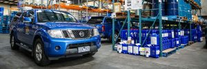 Tandex service vehicles parked inside the factory beside racking stocked with blue chemical containers and industrial supplies.