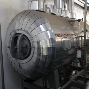 A polished stainless-steel condensate tank connected to a boiler system, showing detailed pipework and insulation fittings within an industrial plant room.