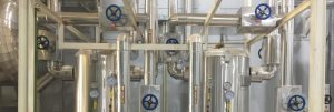 Stainless steel industrial piping system with gauges and valves, possibly part of a closed-loop or hot water circulation system.