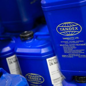 Close-up of blue Tandex chemical drums stacked on storage racking, labelled for industrial water treatment use.