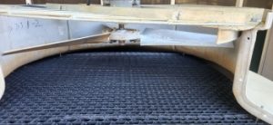 Interior view of a cooling tower showing black plastic drift eliminators beneath the fan assembly, designed to reduce water loss and mist emissions.