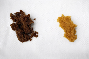 Comparison of water softener resin samples on a white background: clean, amber-coloured resin in good condition on the right, and dark brown, fouled resin in poor condition on the left requiring replacement.
