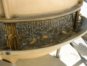 Cooling tower basin with autumn leaf litter and organic debris accumulating in the circulating water beneath the fill pack, increasing fouling and microbiological risk if not removed through routine maintenance.