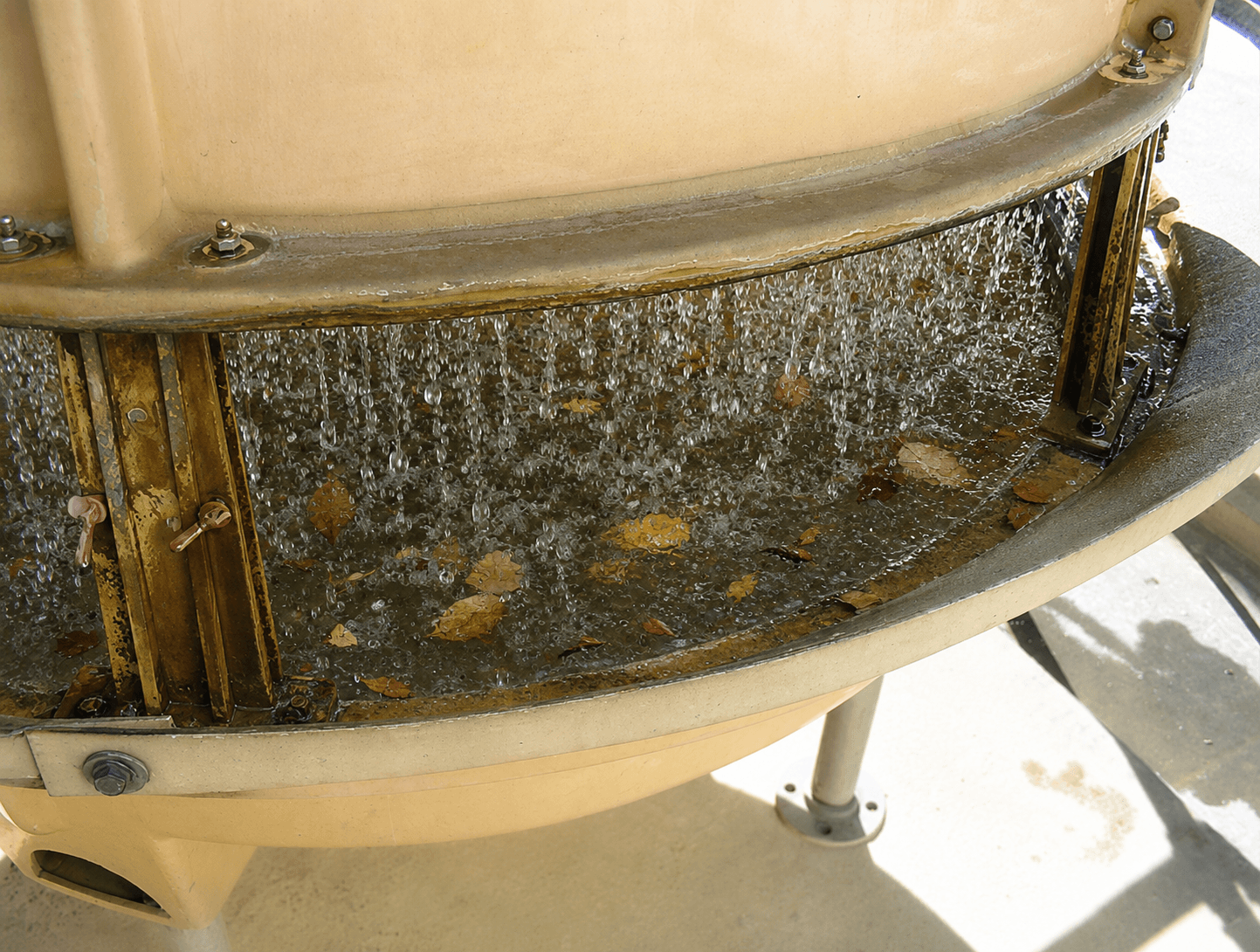 Cooling tower basin with autumn leaf litter and organic debris accumulating in the circulating water beneath the fill pack, increasing fouling and microbiological risk if not removed through routine maintenance.