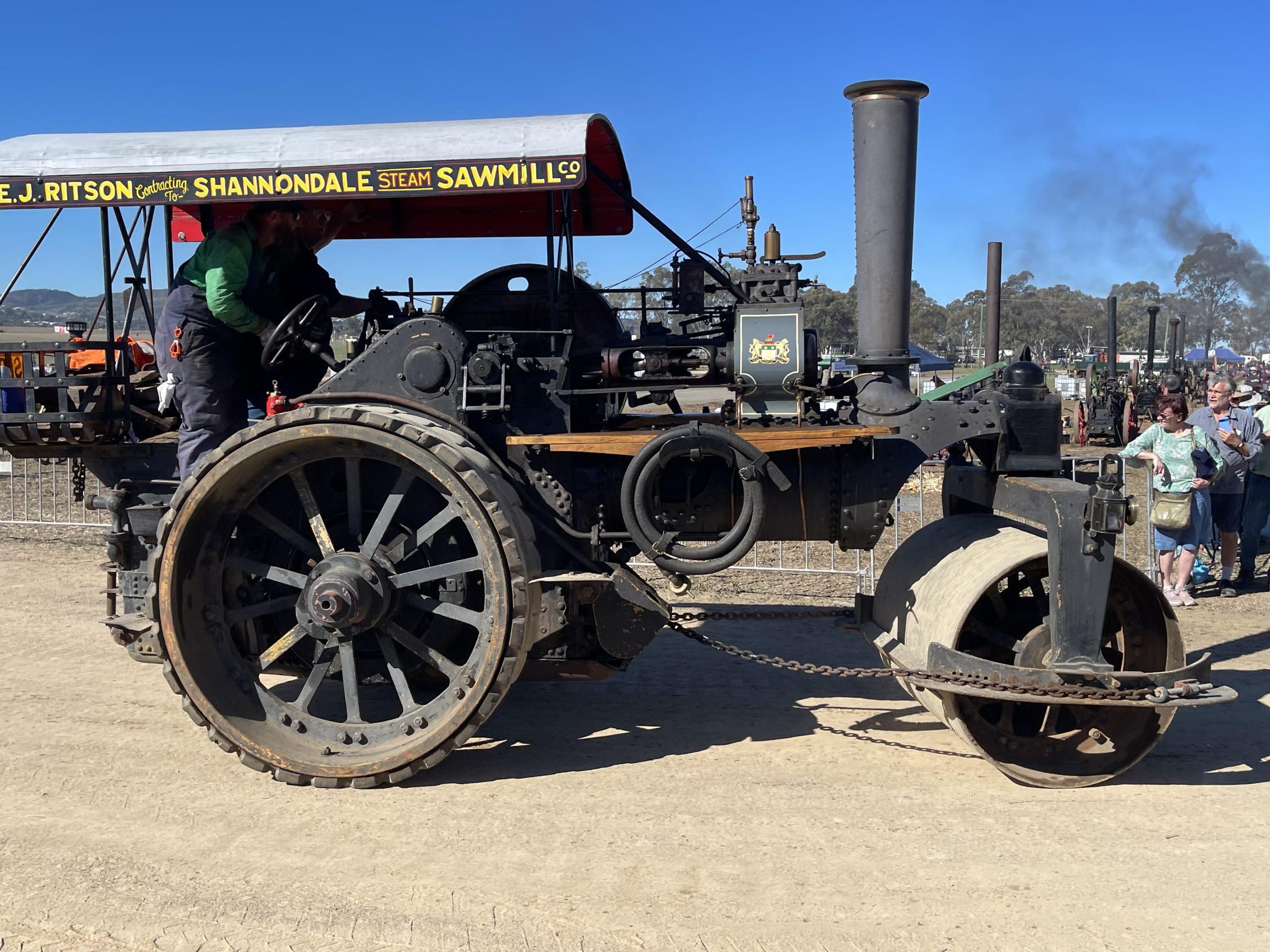 Black steam roller with a red canopy reading “E.J. Ritson Shannondale Steam Sawmill Co” driven along a dirt track during a heritage machinery rally.