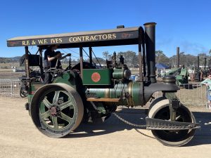 Green and black steam roller labeled “R.F. & W.F. Ives Contractors” being driven along a dirt track at a machinery rally under clear blue skies.