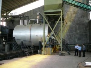 A large industrial boiler installation at a customer site in Indonesia, with three people standing nearby discussing maintenance. The system is maintained by Tandex’s Indonesian agents.