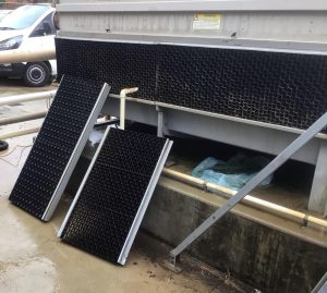 Cooling tower air intake louvres with some panels still installed on the tower and others removed and placed on the ground for cleaning and maintenance.