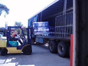 A Tandex factory worker operating a forklift to load pallets of blue chemical drums onto a truck outside the warehouse in 2005.