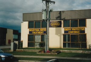 Photograph of the Tandex building taken in 1991 when the facility was purchased, showing signage for industrial water treatment and protective coatings on the front of the building.