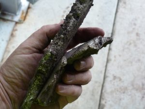 Close-up of a technician’s hand holding very thick, large pieces of hard mineral scale removed from a boiler during inspection, showing severe internal scaling and deposit build-up.