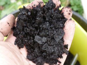Close-up of flaked, black boiler scale held in a technician’s hand after being removed during a routine boiler inspection, showing heavy internal scaling and deposit build-up.