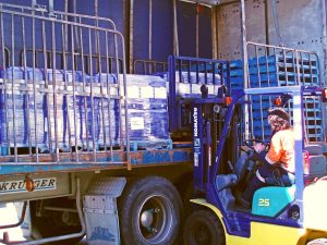A Tandex factory worker operating a forklift to load wrapped pallets of chemical drums onto a truck for export.