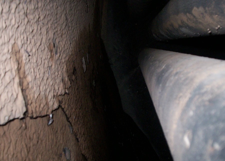 Internal view of a boiler drum showing heavy, cracked mineral scale covering the metal surface prior to treatment, indicating long-term poor boiler water management and significant deposit build-up.