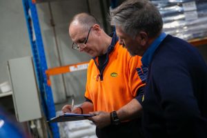 A Tandex factory hand and service technician reviewing and completing a quality control checklist on a clipboard inside the warehouse.