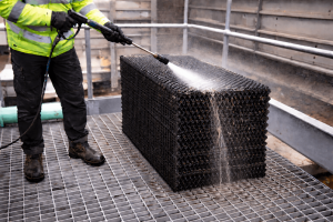 Technician pressure washing fouled cooling tower fill pack as part of a cooling tower super clean to remove biological growth and debris.